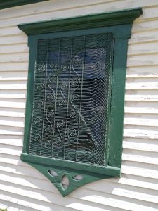 ornate green screen on a window on a small old barn with curliques on the left, and swooping wire crosshatched on the right